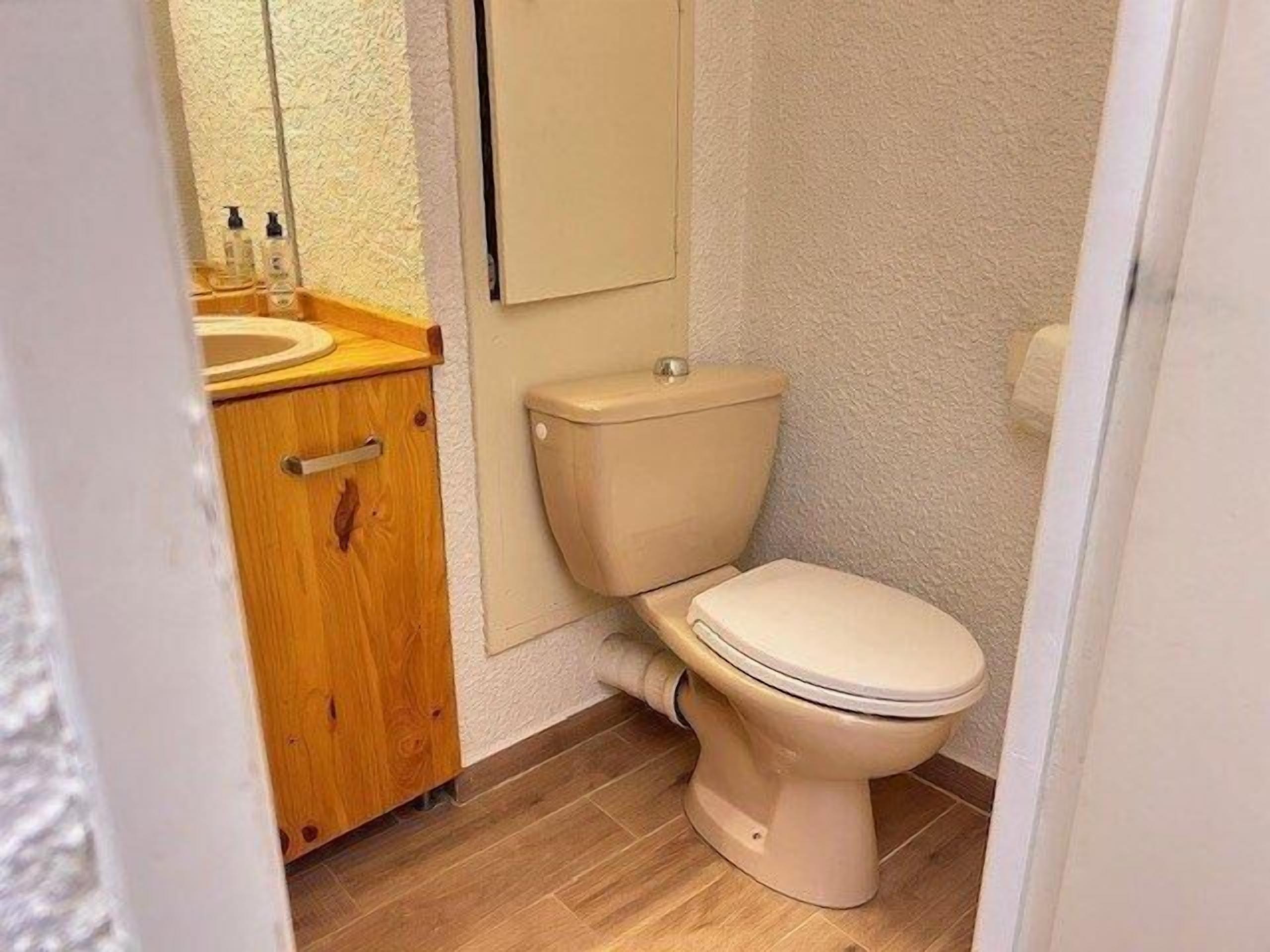 A small bathroom with a toilet, wooden cabinet, and a mirror.