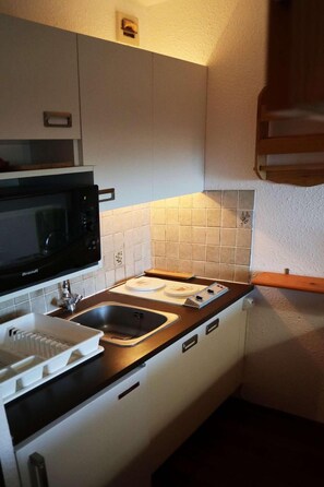 A compact kitchen with a Brandt microwave, a sink, and a stovetop.