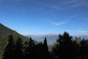 A mountainous landscape with dense forest in the foreground and distant mountain ranges under a clear sky.