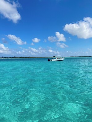 Un bote en aguas turquesas cristalinas, con una costa lejana y un cielo azul despejado.