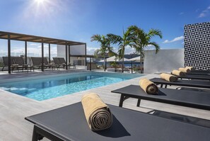 Un área de piscina en la azotea con sillones de descanso y una zona de estar cubierta, con vistas a una masa de agua.