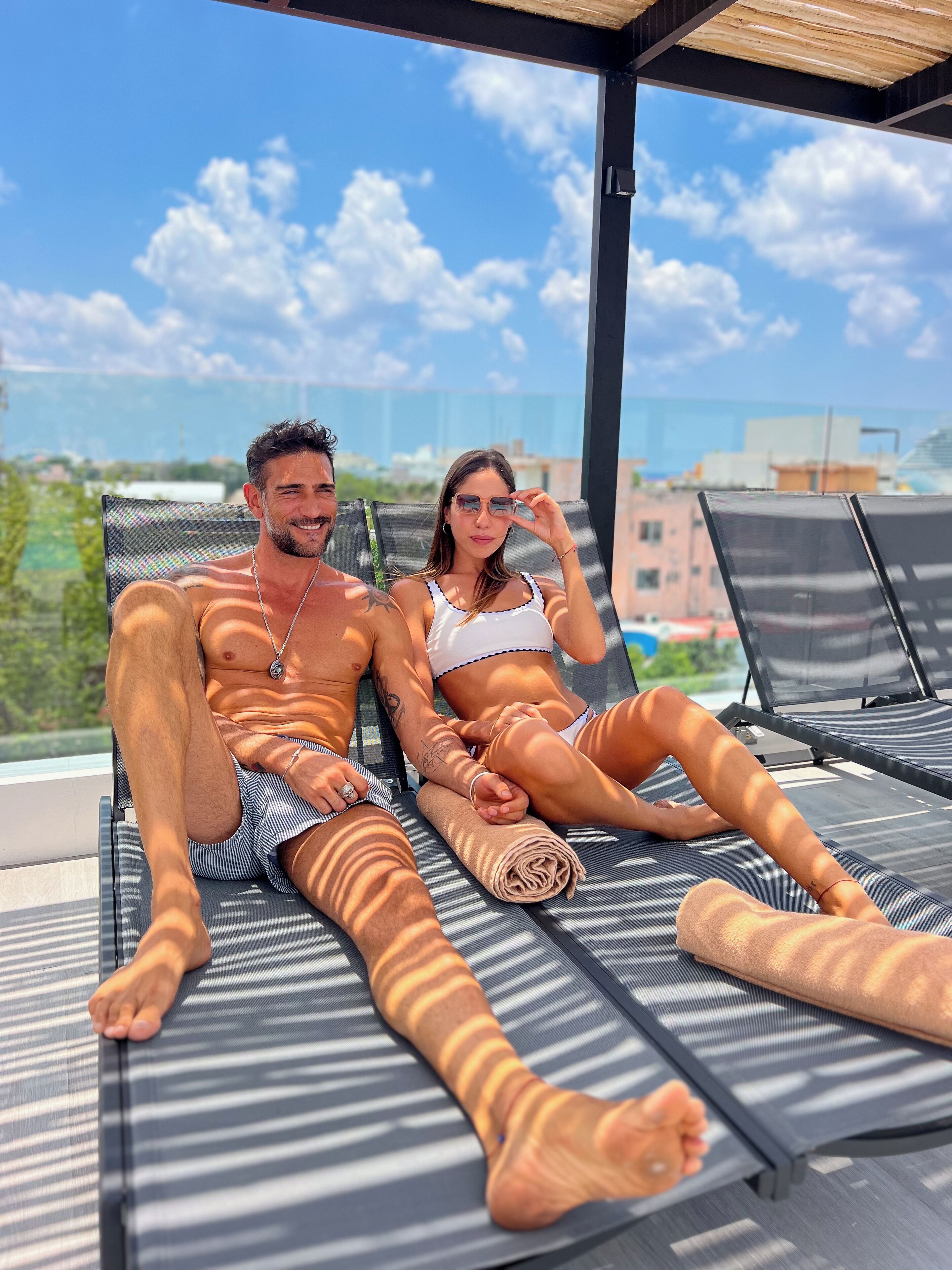 Two people reclining on sun loungers with a cityscape and greenery in the background.