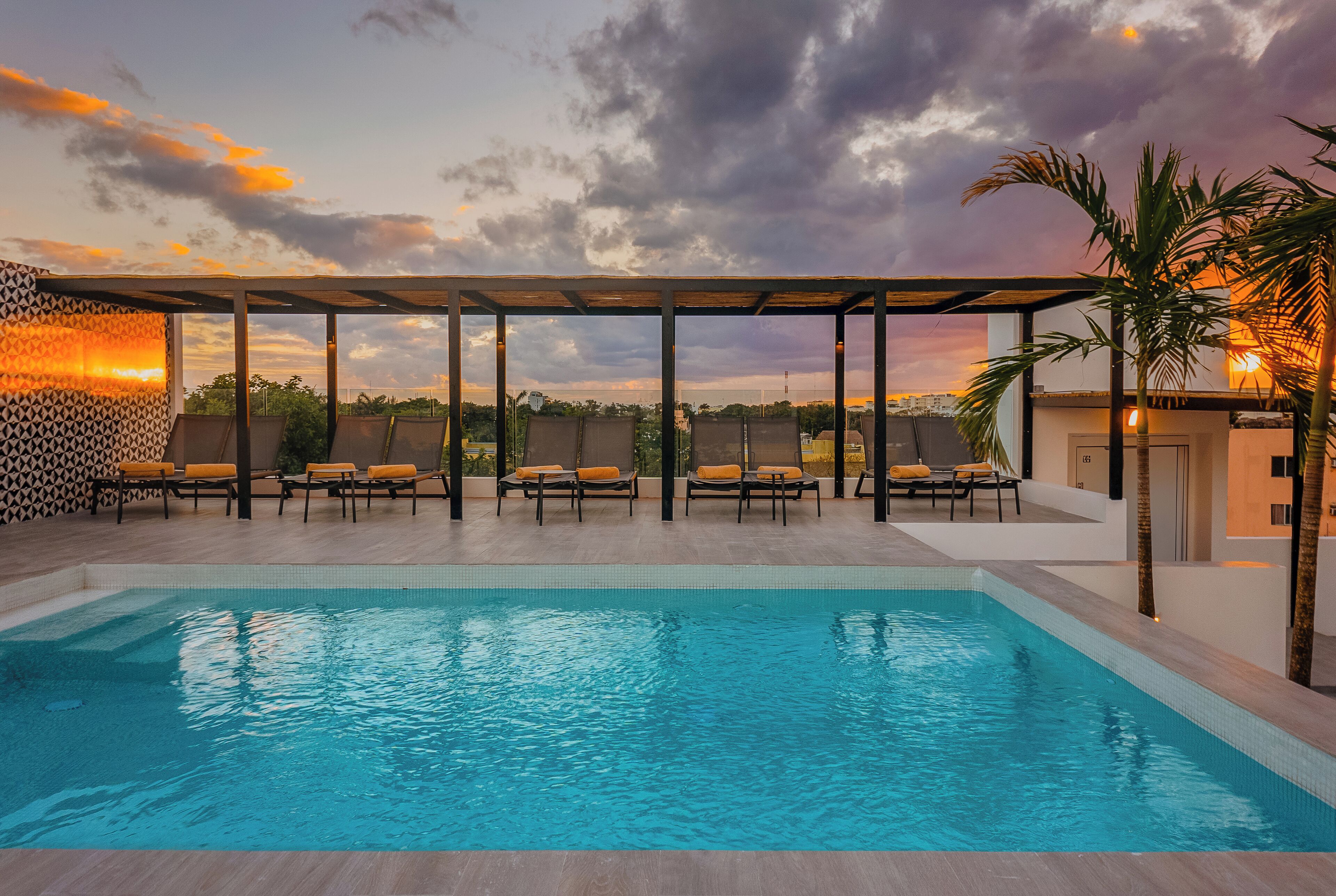 Une piscine avec des chaises longues et une pergola, le tout baigné par la lumière d’un coucher de soleil.