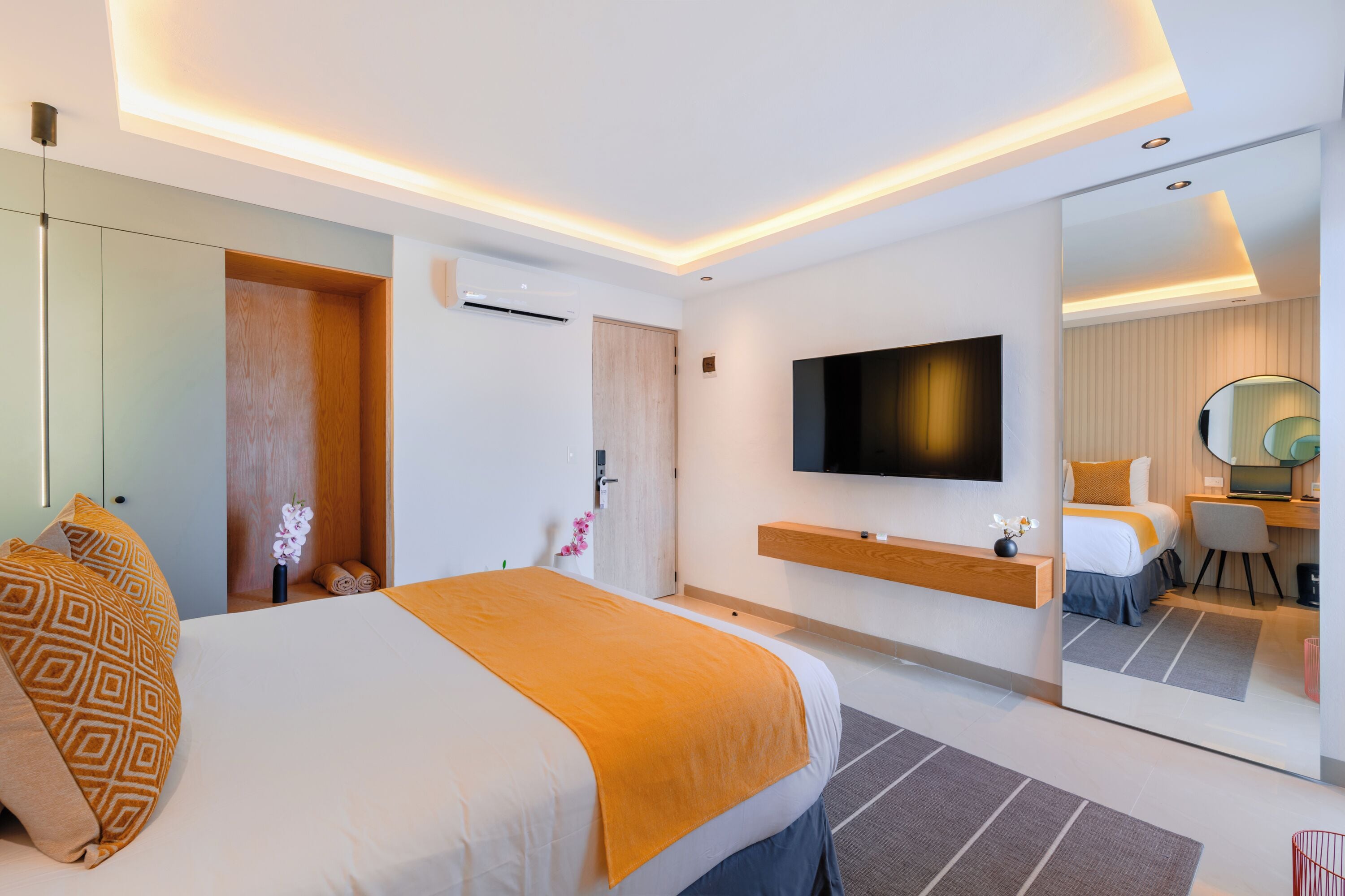 A modern hotel room with a large bed, a flat-screen TV, a mirror, and a desk with a chair.