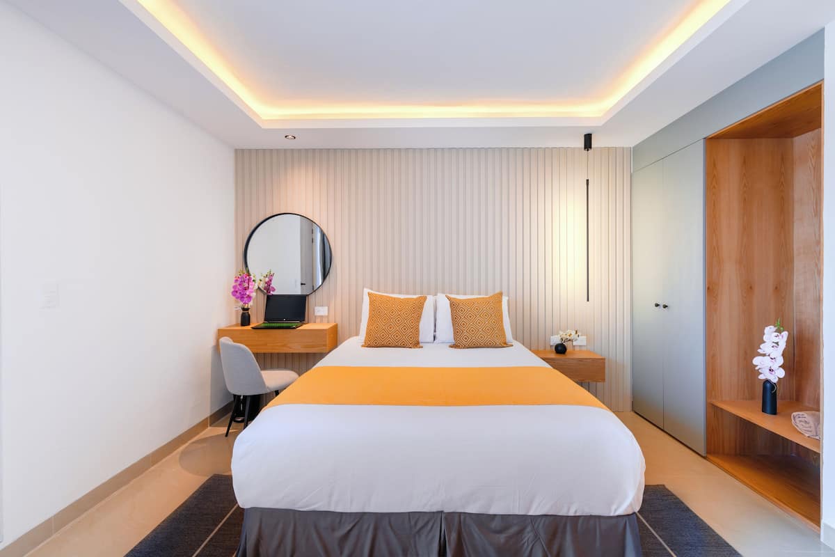 Ein modernes Hotelzimmer mit einem großen Bett, einem Schreibtisch mit Computer, einem Spiegel und einem Holzschrank.