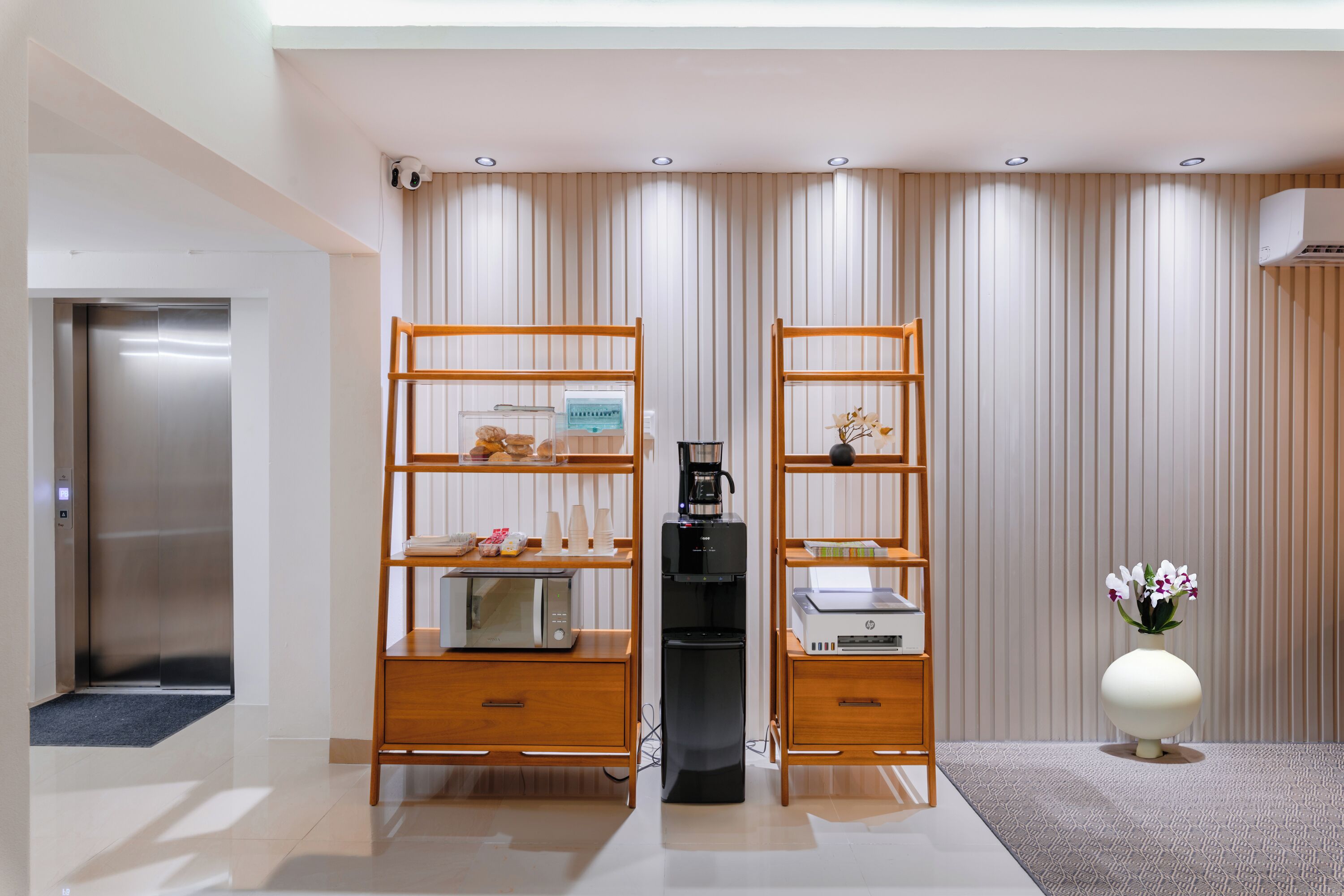 A modern hotel room with a wooden desk, a coffee machine, a microwave, and a printer.