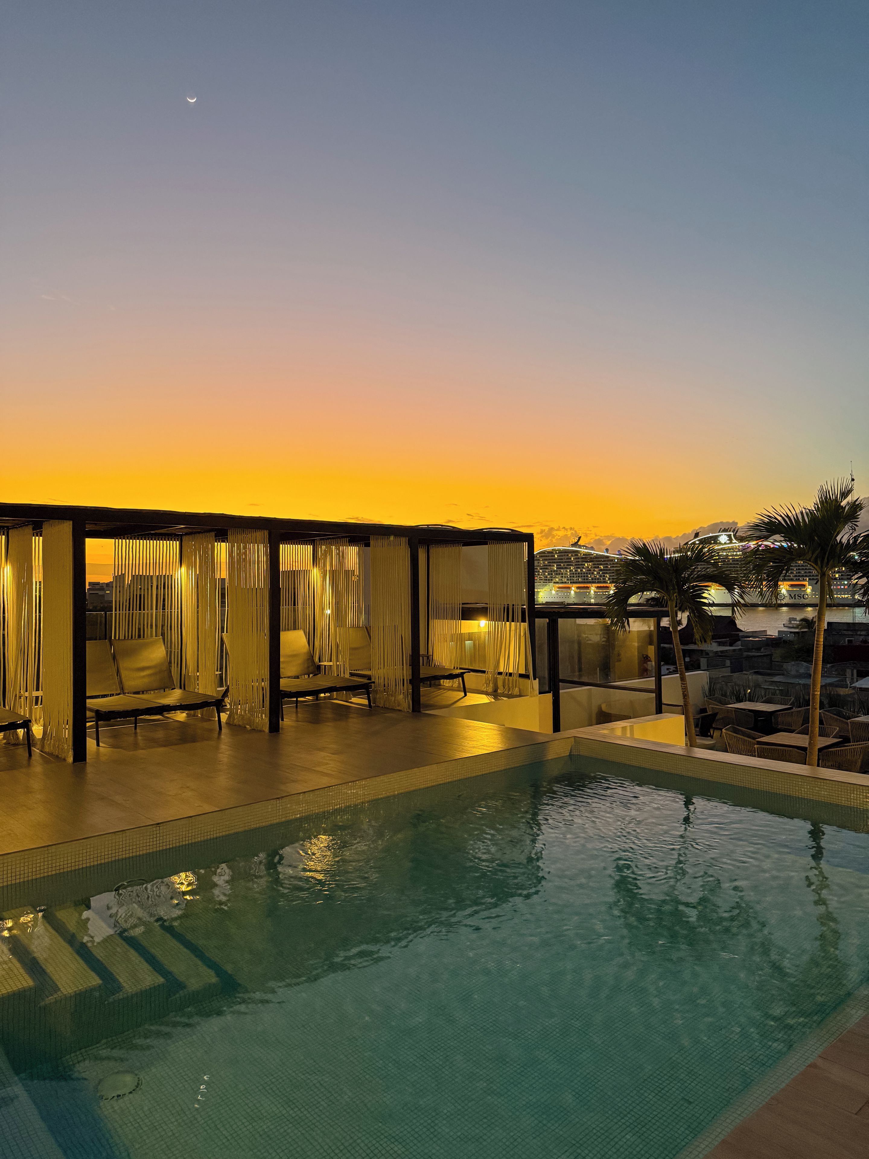 Un área de piscina con sillones de descanso y vistas al atardecer.