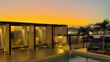 Un área de piscina con sillones de descanso y vistas al atardecer.