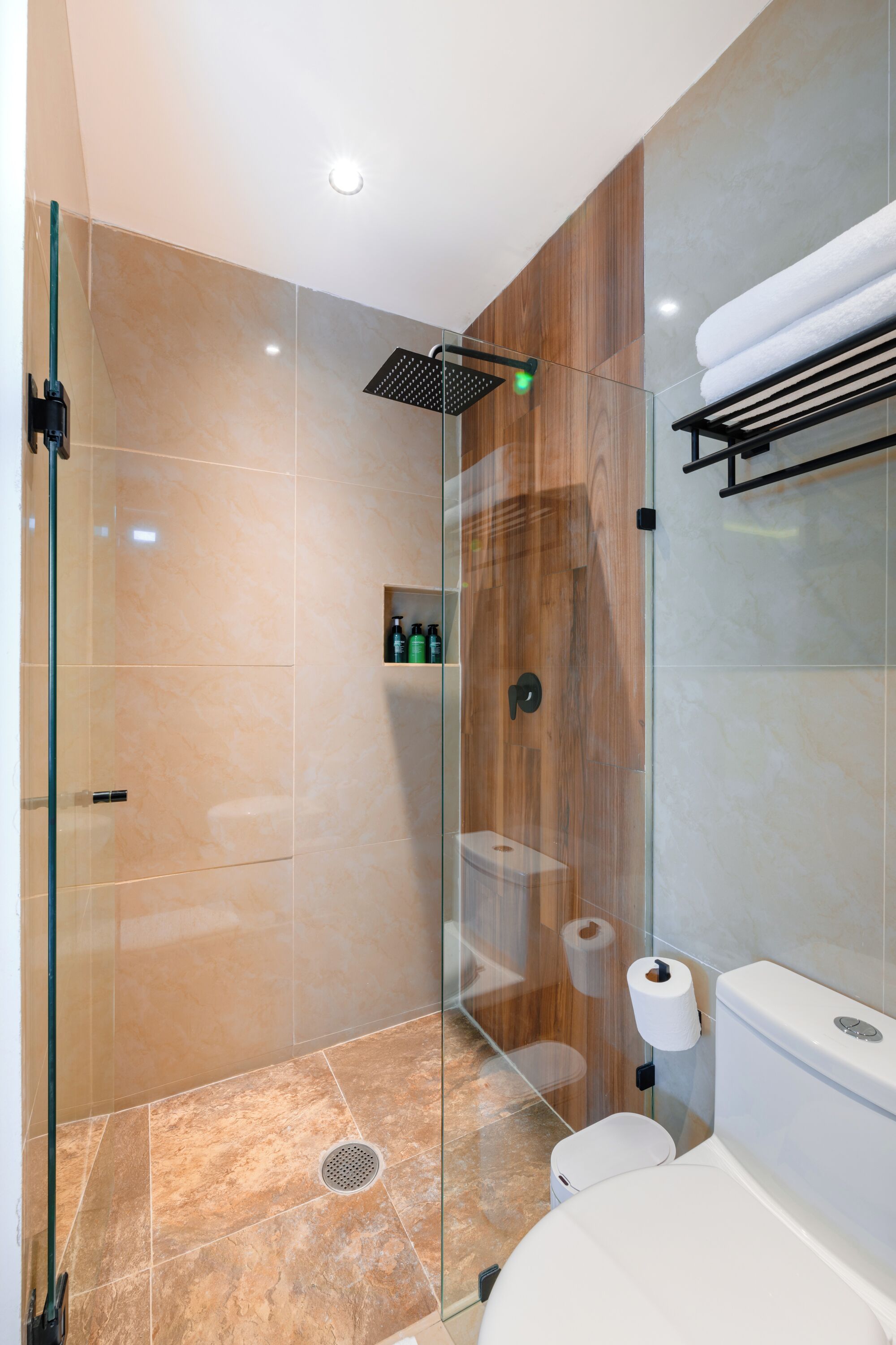 A modern bathroom with a glass-enclosed shower, a toilet, and a built-in shelf with toiletries.