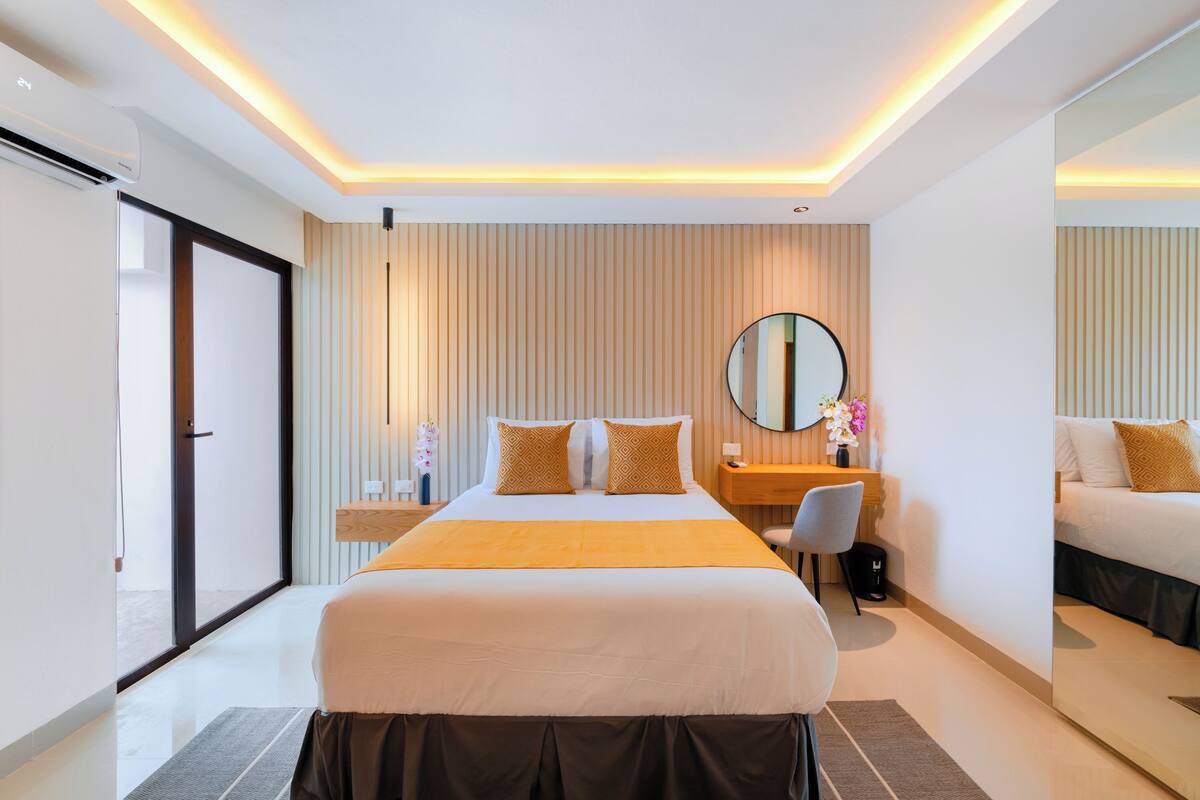 Ein modernes Hotelzimmer mit einem großen Bett, einem Schreibtisch, einem Stuhl, einem Spiegel und einer Schiebetür links.