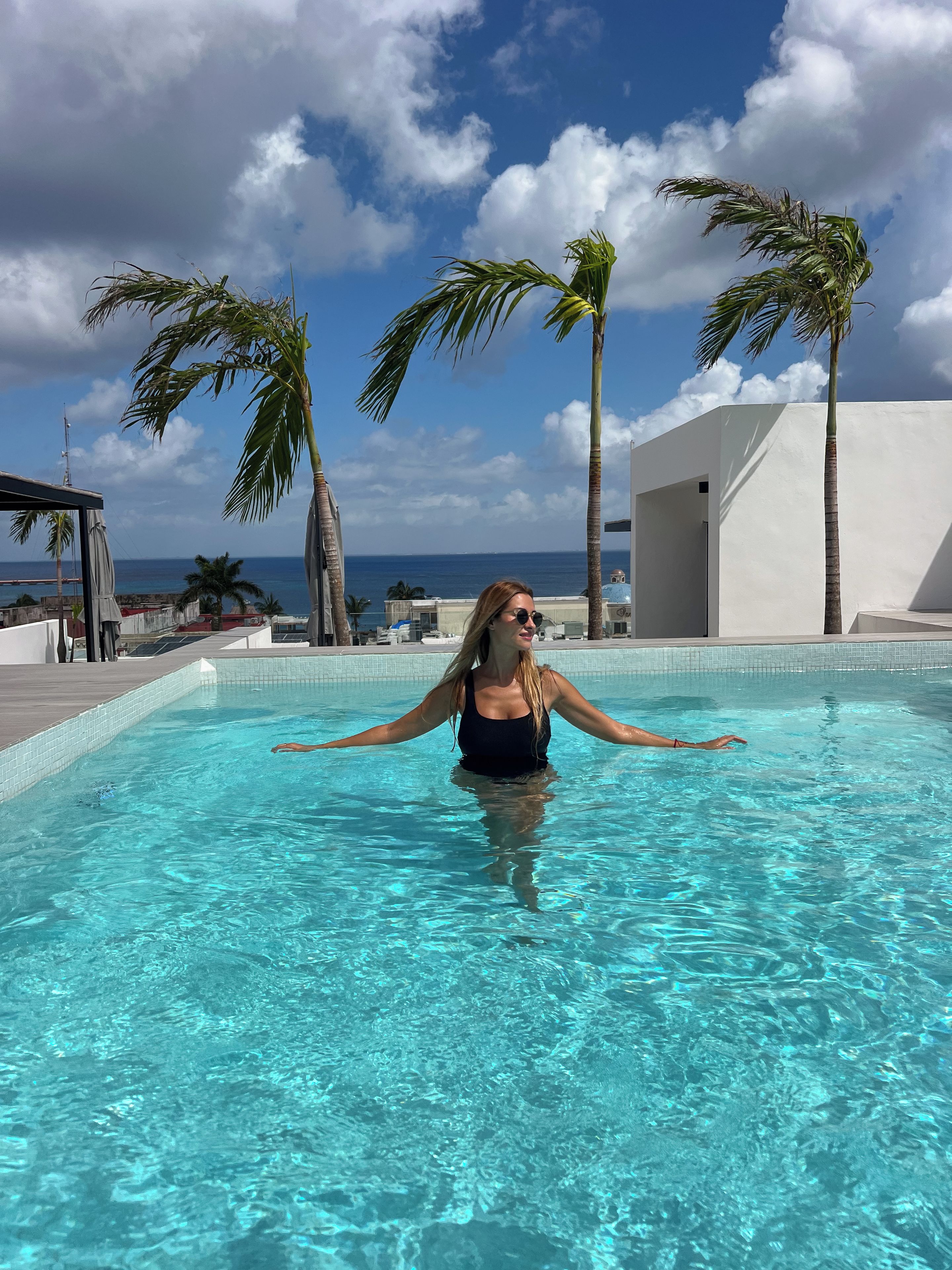 Une personne dans une piscine, avec vue sur l’océan et les palmiers.