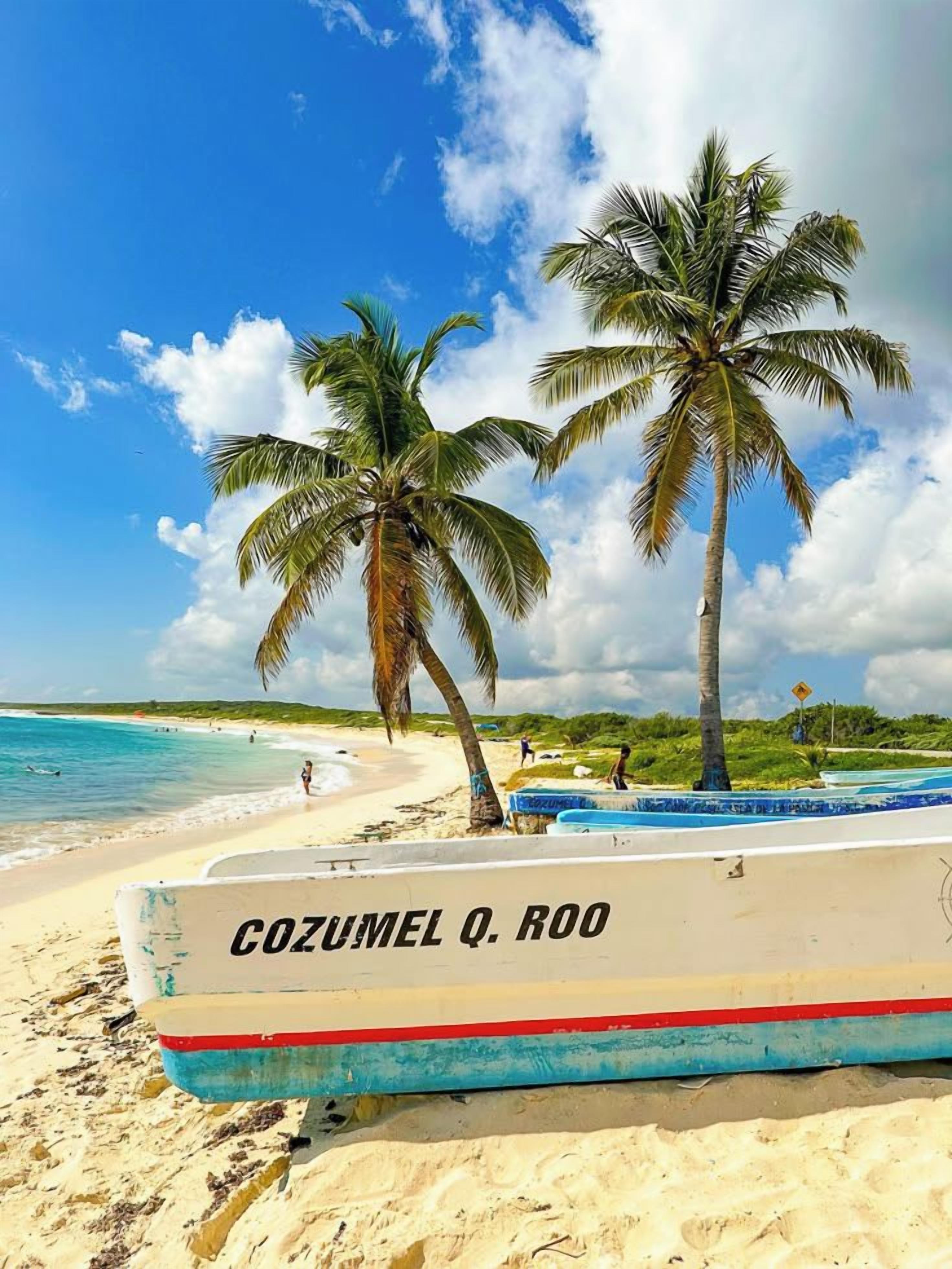 Une plage avec un bateau appelé « COZUMEL Q. ROO » et des palmiers.