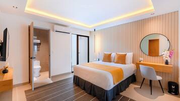 A modern hotel room with a large bed, a desk, a chair, a mirror, and a bathroom visible through an open door.
