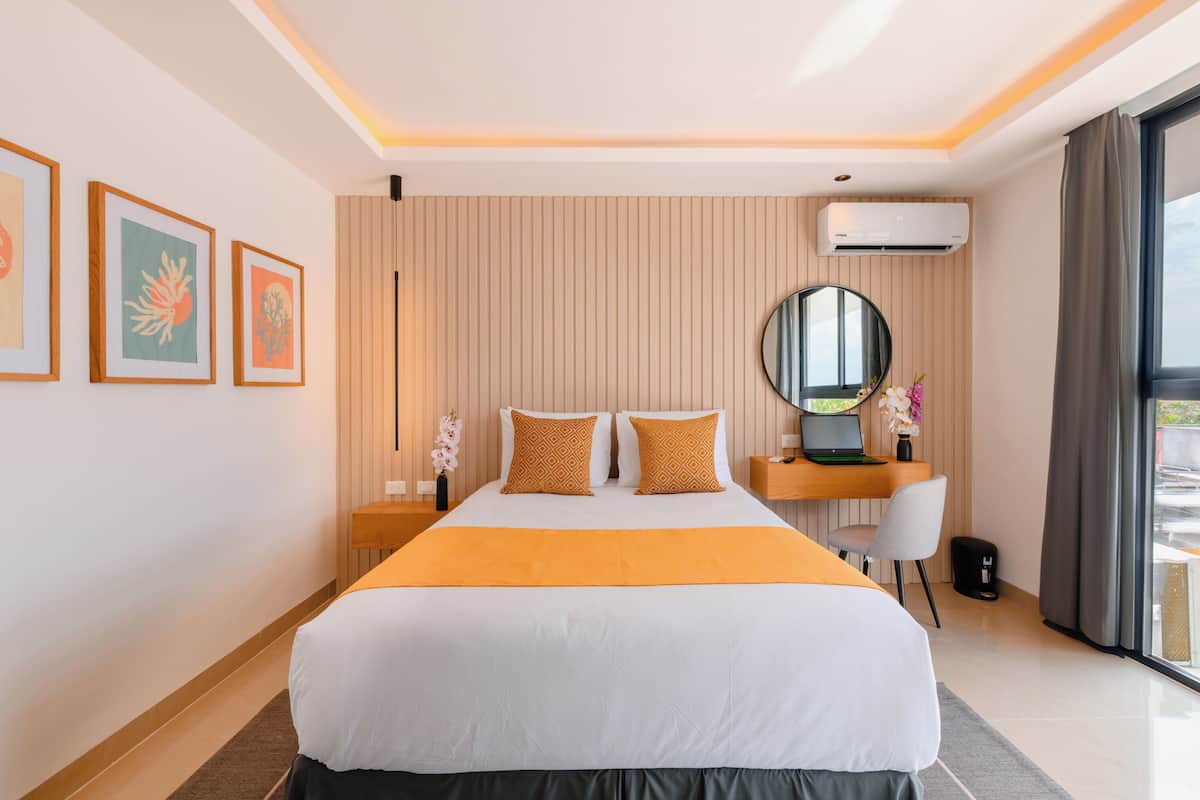 Ein modernes Hotelzimmer mit einem großen Bett, einem Schreibtisch mit einem Laptop, einem runden Spiegel und einem Fenster mit Vorhängen.