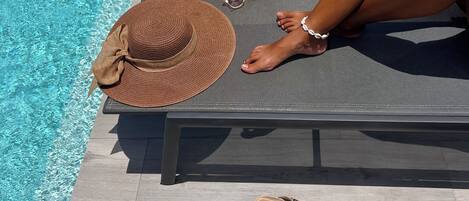 Un espace aménagé au bord de la piscine, avec un fauteuil de relaxation, une serviette enroulée, un chapeau, des lunettes de soleil et des sandales.