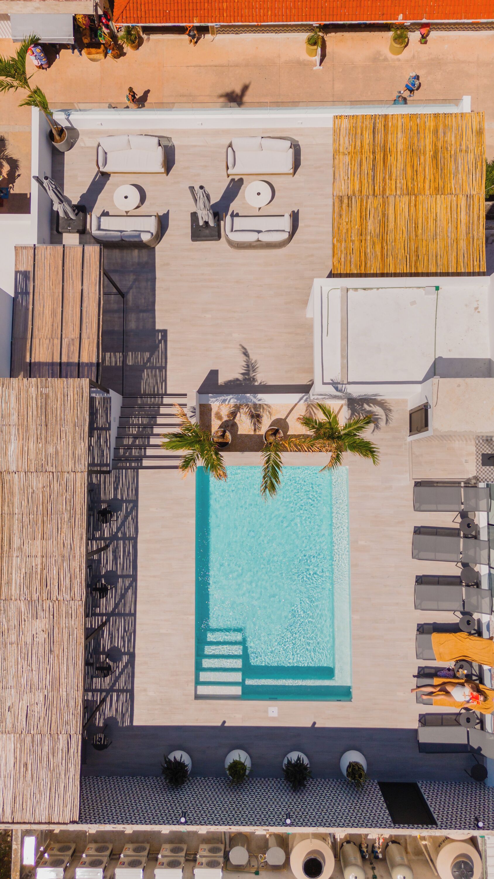An aerial view of a rooftop pool area with lounge chairs, a pool, and a wooden deck.