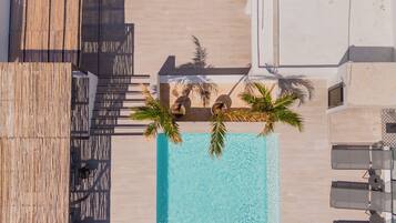 An aerial view of a rooftop pool area with lounge chairs, a pool, and a wooden deck.