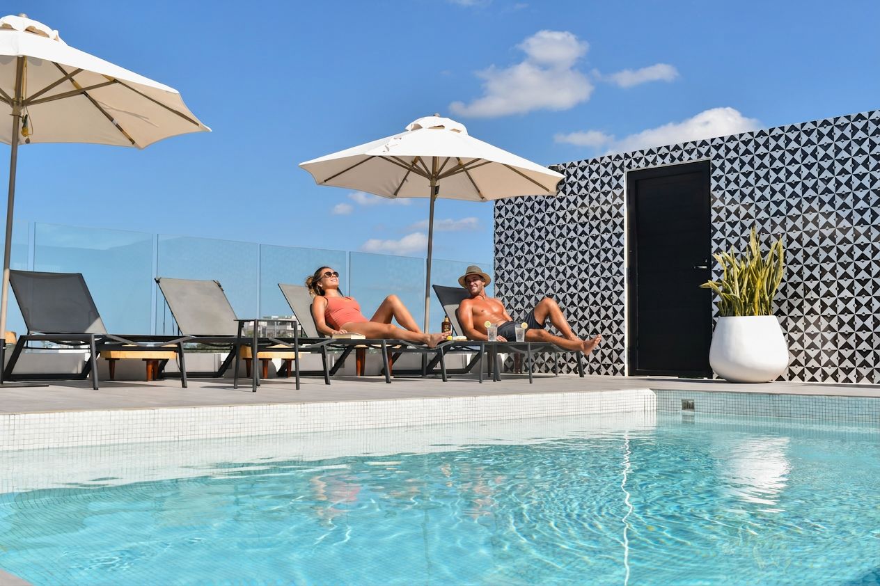 A poolside area with lounge chairs and umbrellas, a tiled pool, and a patterned wall.