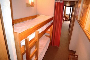 A bunk bed room with a wooden headboard, a small shelf with a light, and a red curtain.