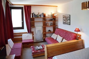 A cozy living room with a sofa, two armchairs, a small table, and a bookshelf filled with books and decorative items.