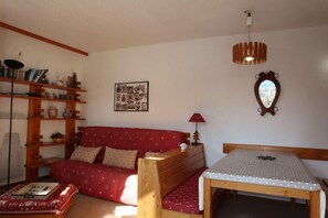 A cozy living room with a red sofa, wooden shelves, a dining table, and a mirror.