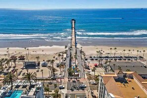 A coastal hotel with a long pier extending into the ocean, a beach area with palm trees, and a parking lot. - Brand New Beach House Fun, Stroll to Downtown, Steps to Beach (Oceanside)