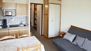 Habitació senzilla amb cuina americana, taula de dinar i cadirees, i sofà.
