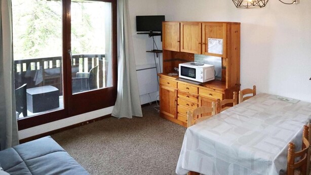 Habitació compacta amb sofà, taula de dinar, petita cuina amb microones i televisió.