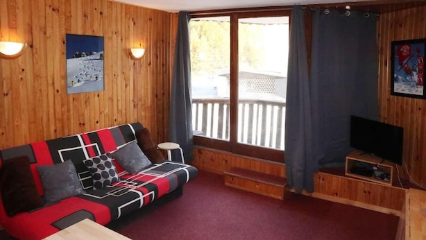Ein Zimmer mit Holzwänden, einer Couch, einem Fernseher und einem Fenster mit Vorhängen.