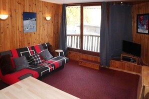 A wooden-paneled room with a sofa, a television, and a window with curtains. - 15m from ski slopes, 6th floor, view ski slopes, balcony, 20m², Les Orres (Les Orres)