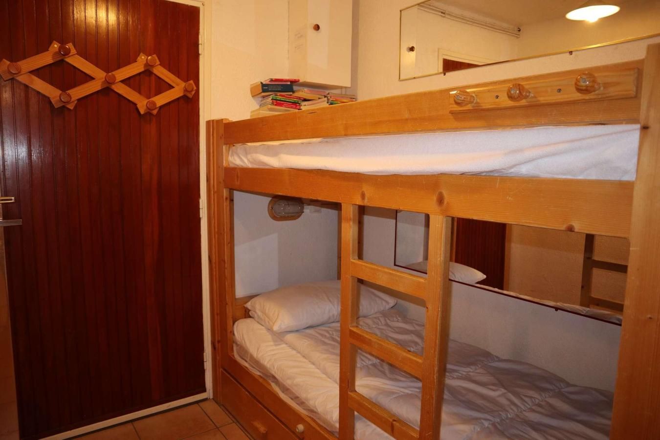 A bunk bed room with a wooden wardrobe and a mirror on the wall.