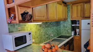 A compact kitchen with wooden cabinets, a microwave, a sink, and a green tiled backsplash.