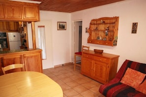 A compact kitchen with wooden cabinets, a dining table, and a red cushioned sofa.