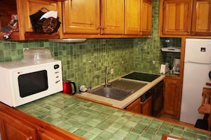 A kitchen with wooden cabinets, a green tiled backsplash, a white microwave, a sink, and a refrigerator.