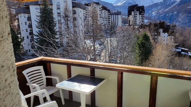 A balcony with a table and chairs, overlooking a mountainous landscape with buildings.