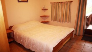 A bedroom with a bed, a nightstand, a shelf, a window with curtains, and a painting on the wall.