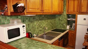 A kitchen with wooden cabinets, a green tiled backsplash, a white microwave, a sink, and a refrigerator.