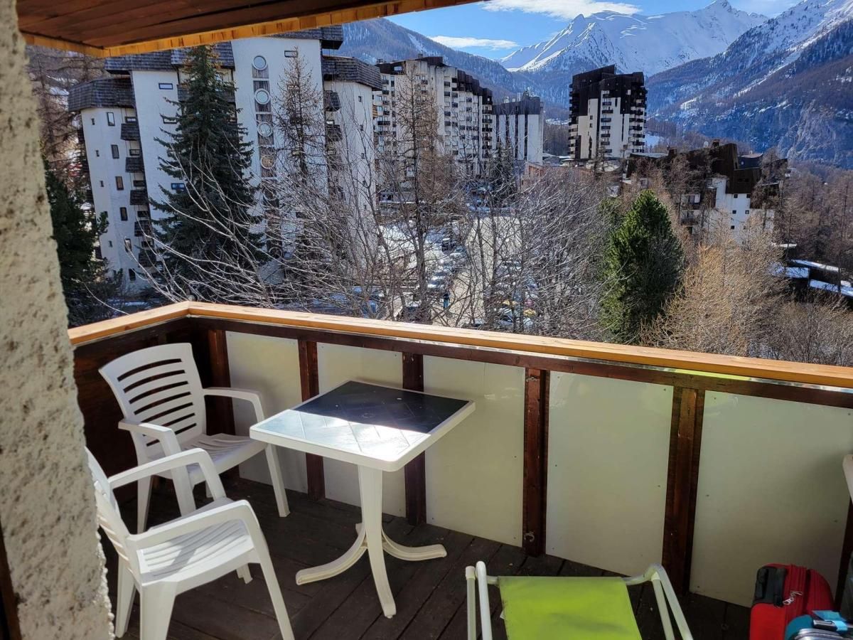 A balcony with a table and chairs, overlooking a mountainous landscape with buildings.