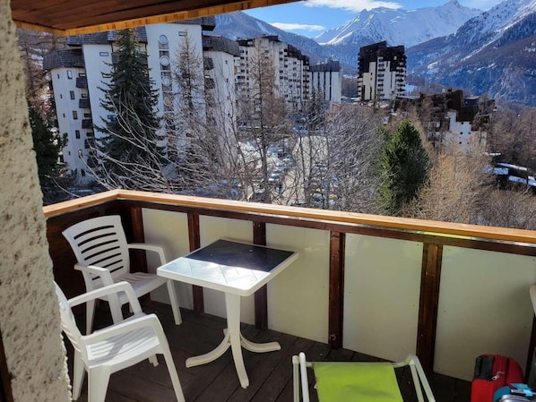 A balcony with a table and chairs, overlooking a mountainous landscape with buildings.