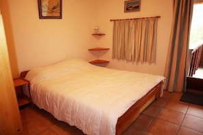 A bedroom with a bed, a nightstand, a shelf, a window with curtains, and a painting on the wall.