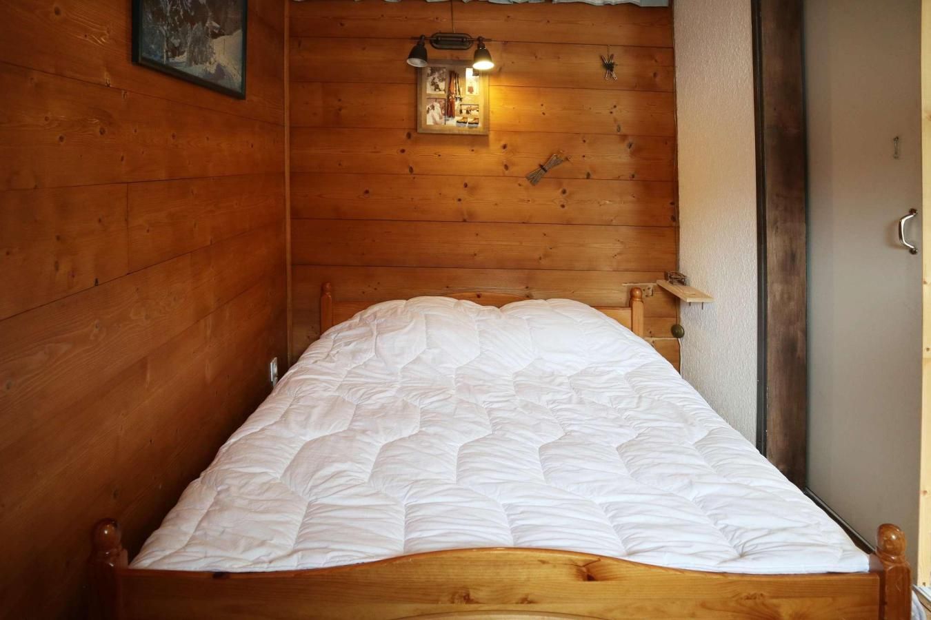 A wooden room with a bed, a small wall-mounted light, and a door.