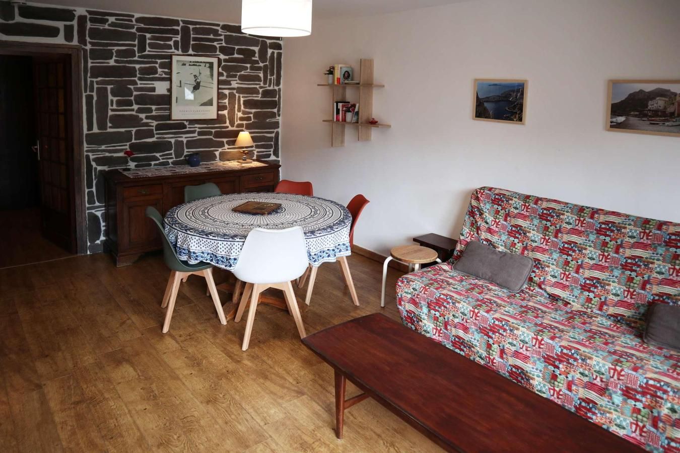 Una sala acogedora con una mesa redonda, un sofá estampado y una pared de piedra.