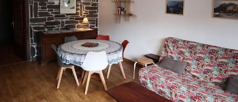Una sala acogedora con una mesa redonda, un sofá estampado y una pared de piedra.