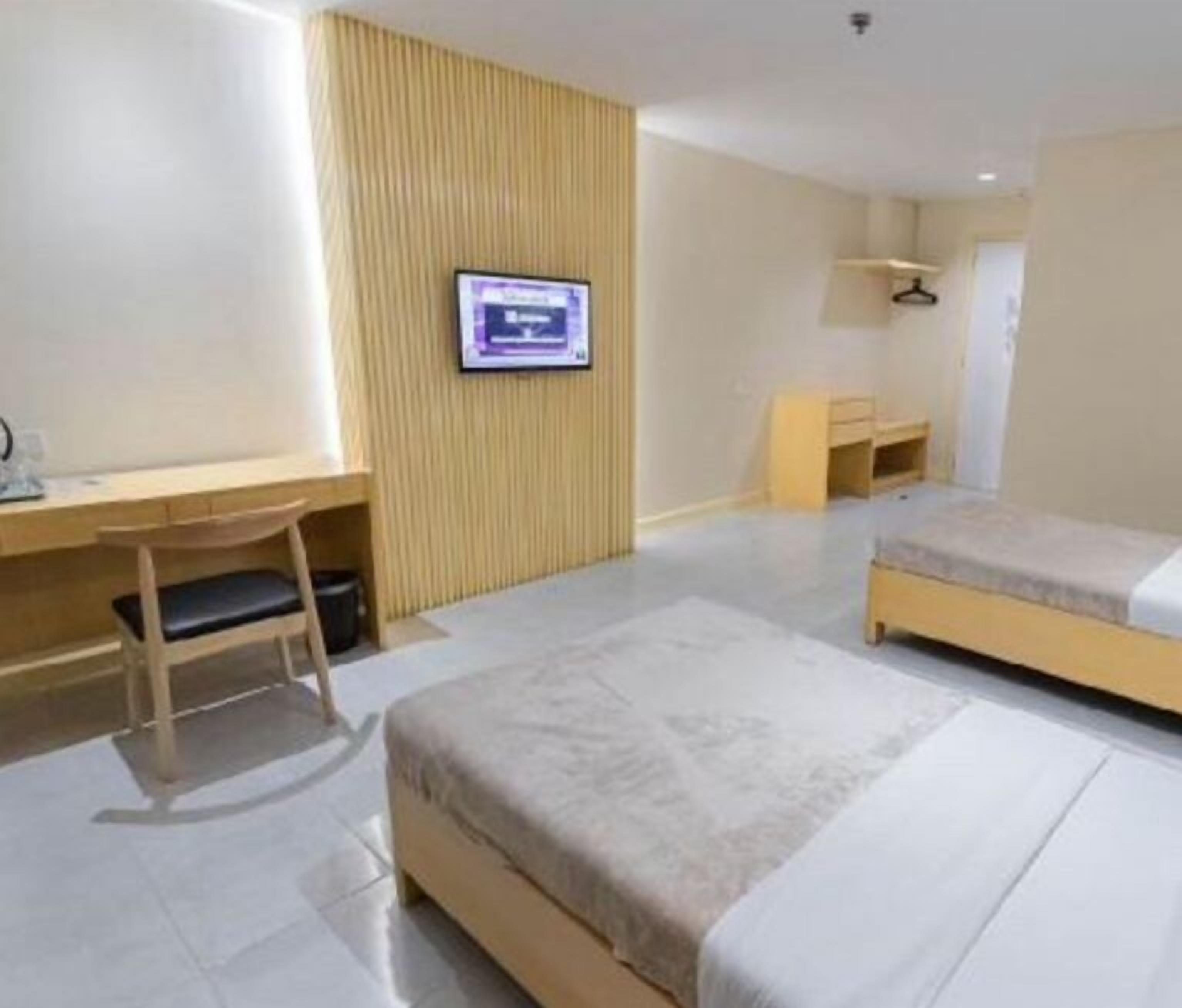 A hotel room with a bed, a desk, a chair, a television, and a wardrobe.