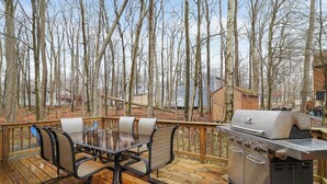 A wooden deck with a grill and dining table with chairs. - Cabin in the heart of Poconos! A Pocono Bliss! Close to Kalahari and Camelback (Tobyhanna)