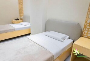 Ein Hotelzimmer mit zwei Einzelbetten, einem Nachttisch mit Lampe und einem kleinen Beistelltischchen mit Telefon.