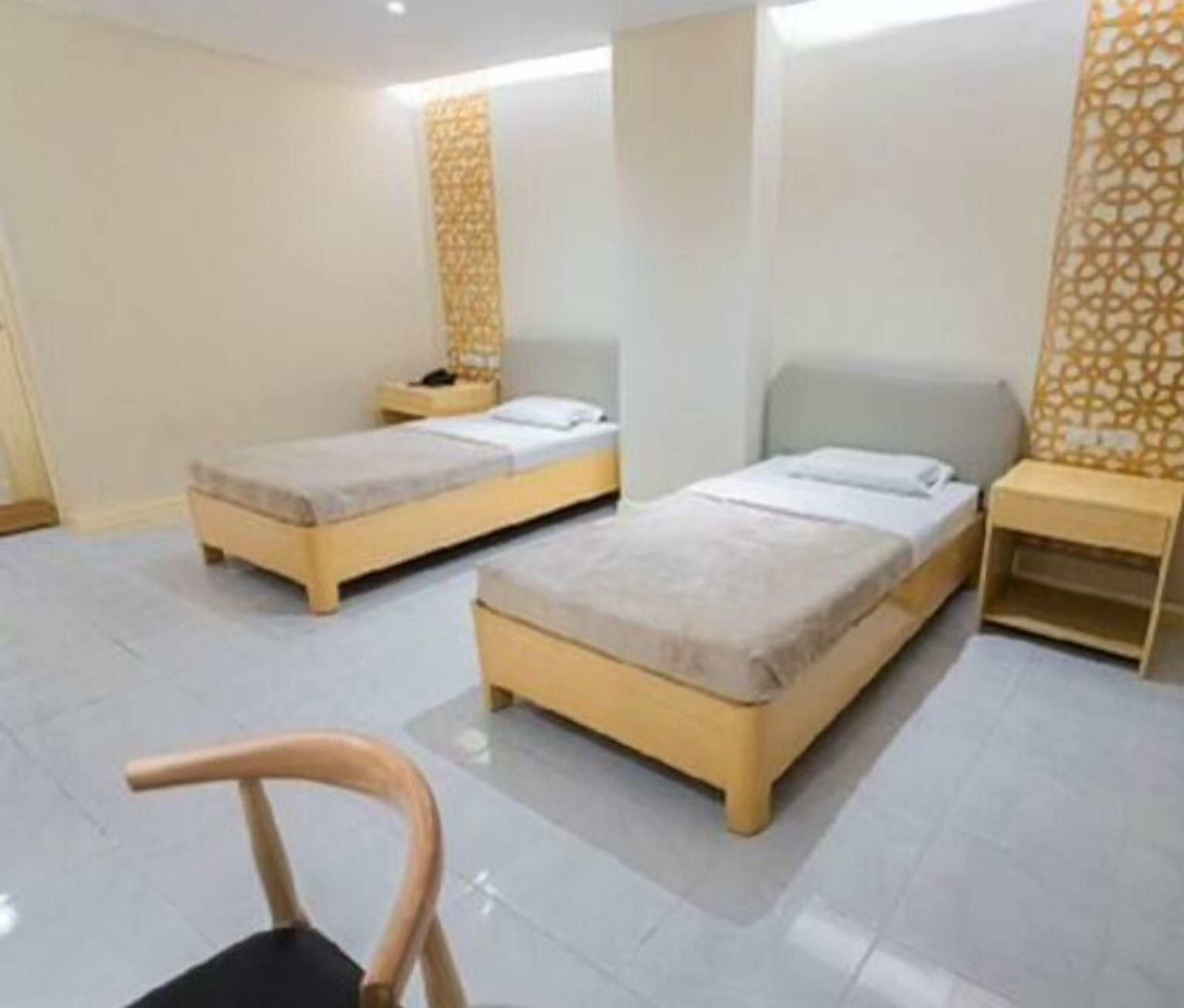 A hotel room with two single beds, a small table, a chair, and a decorative wall panel.