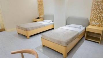 A hotel room with two single beds, a small table, a chair, and a decorative wall panel.