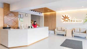 Un espace d’accueil d’hôtel au design moderne, comprenant un comptoir d’accueil, un réceptionniste et un logo affiché sur le mur.