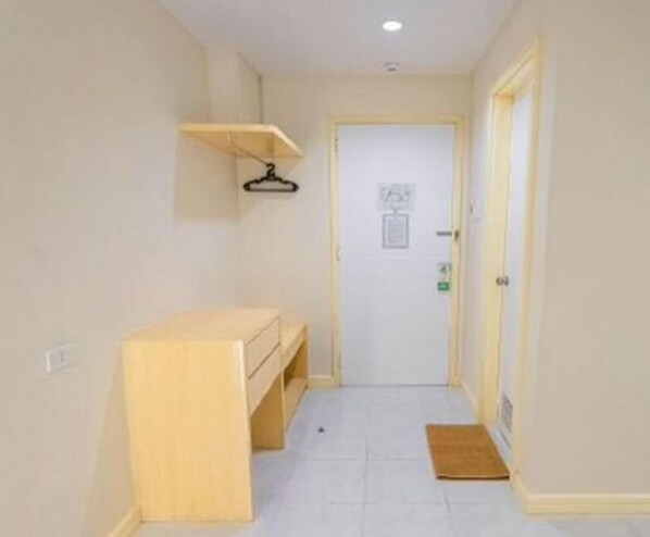Un pasillo estrecho con un banco de madera, una puerta con un cartel y un tapete pequeño en el suelo.